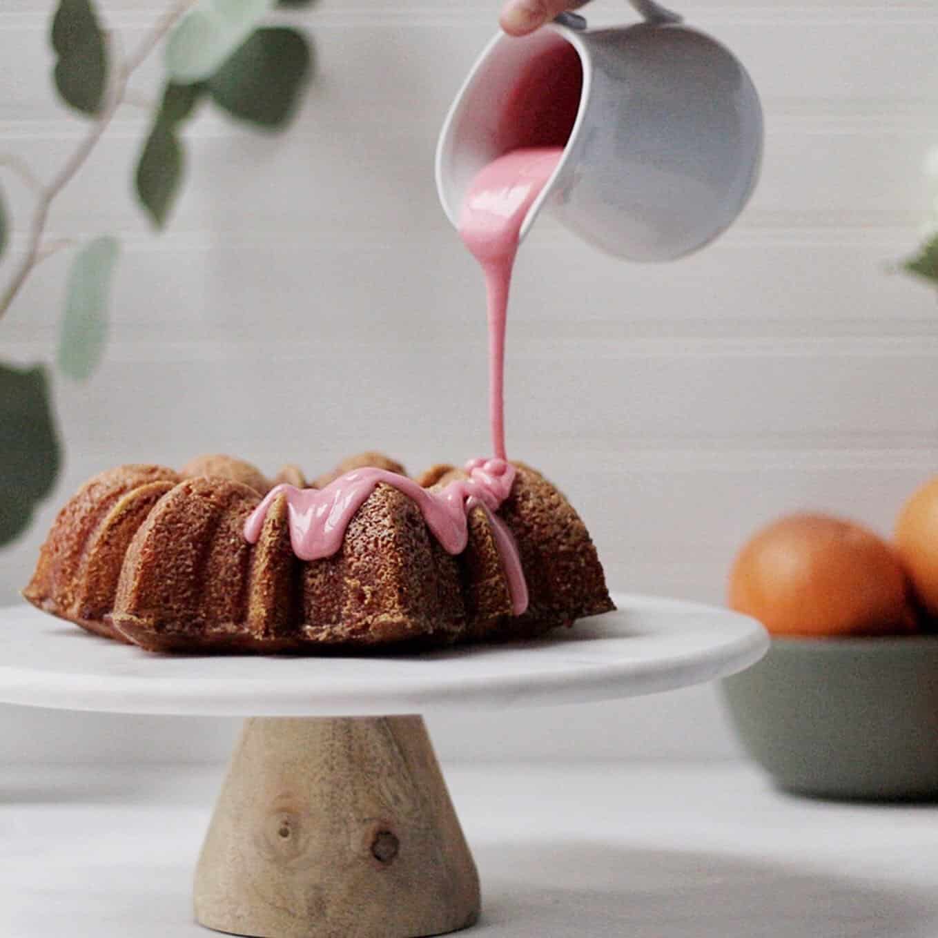 bundt cake on marble cake stand with pink blood orange icing being poured 