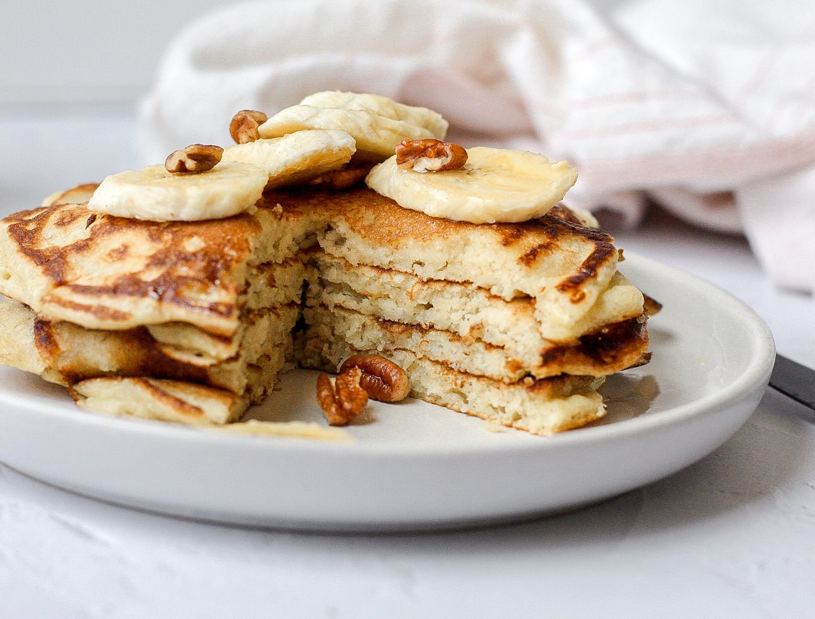 sourdough pancakes with a slice cut out topped with sliced banana and pecans