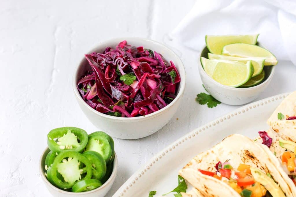 bowl of fresh cabbage slaw with jalapenos and lime wedges