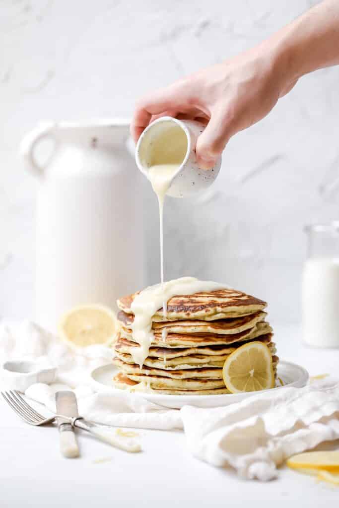 lemon poppy seed sourdough pancakes  with icing being poured on top