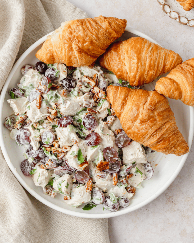 A close up of a bowl of chicken salad with croissants 