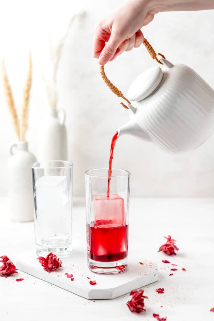 pouring hibiscus rose tea into glass with ice