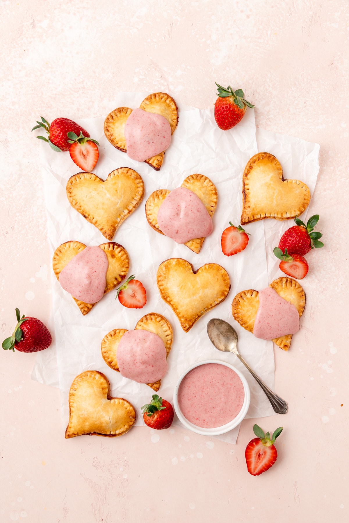 heart shaped strawberry hand pies on parchment with pink glaze.