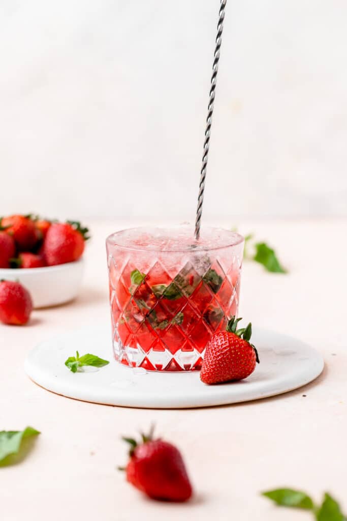 stirring strawberry basil mojito in glass.