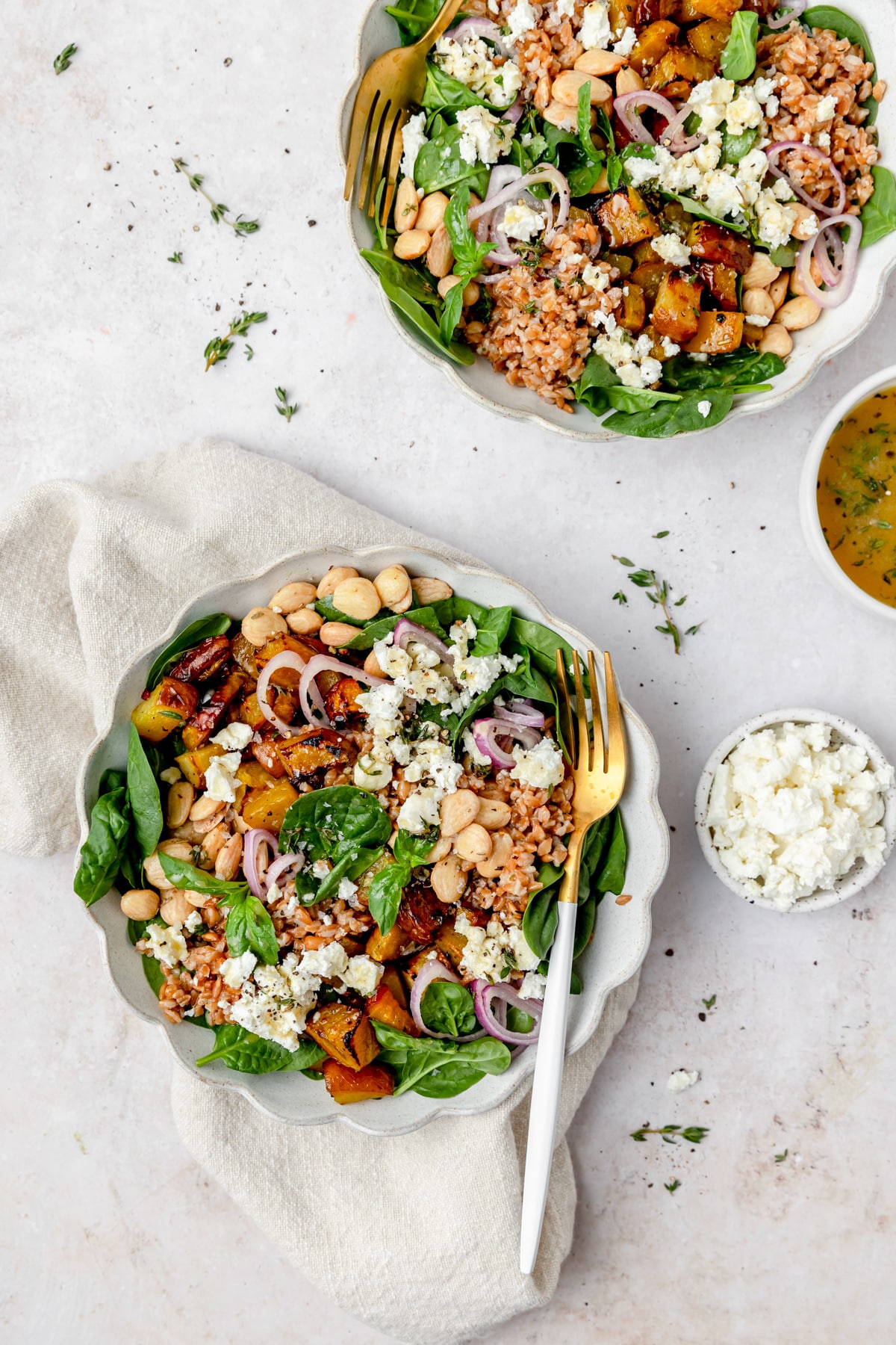 two bowls of spinach salad with roasted golden beets, goat cheese, and farro.