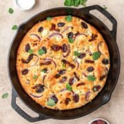 close up shot of cast iron focaccia with sundried tomatoes and Kalamata olives.