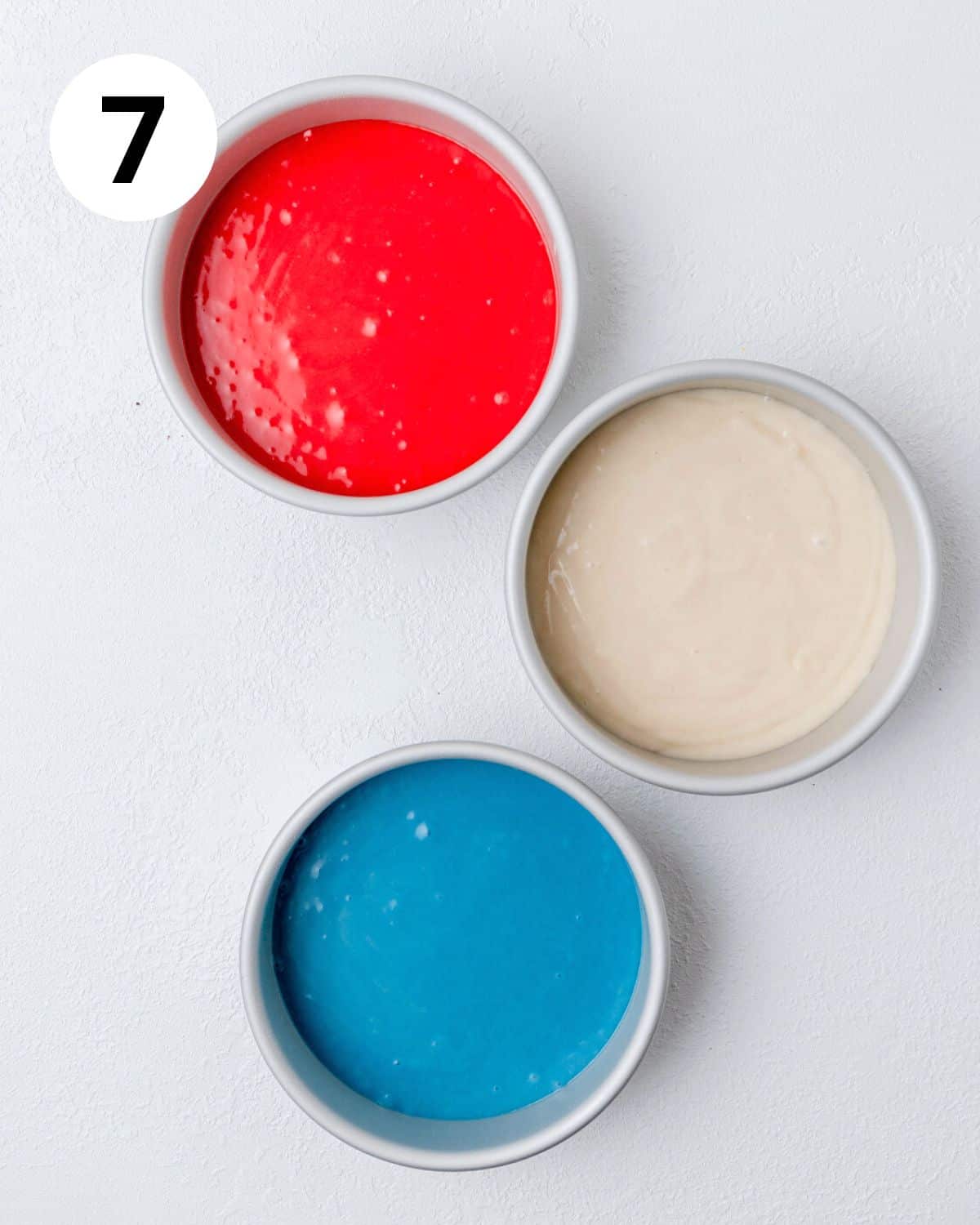 different color cake batters in cake pans.