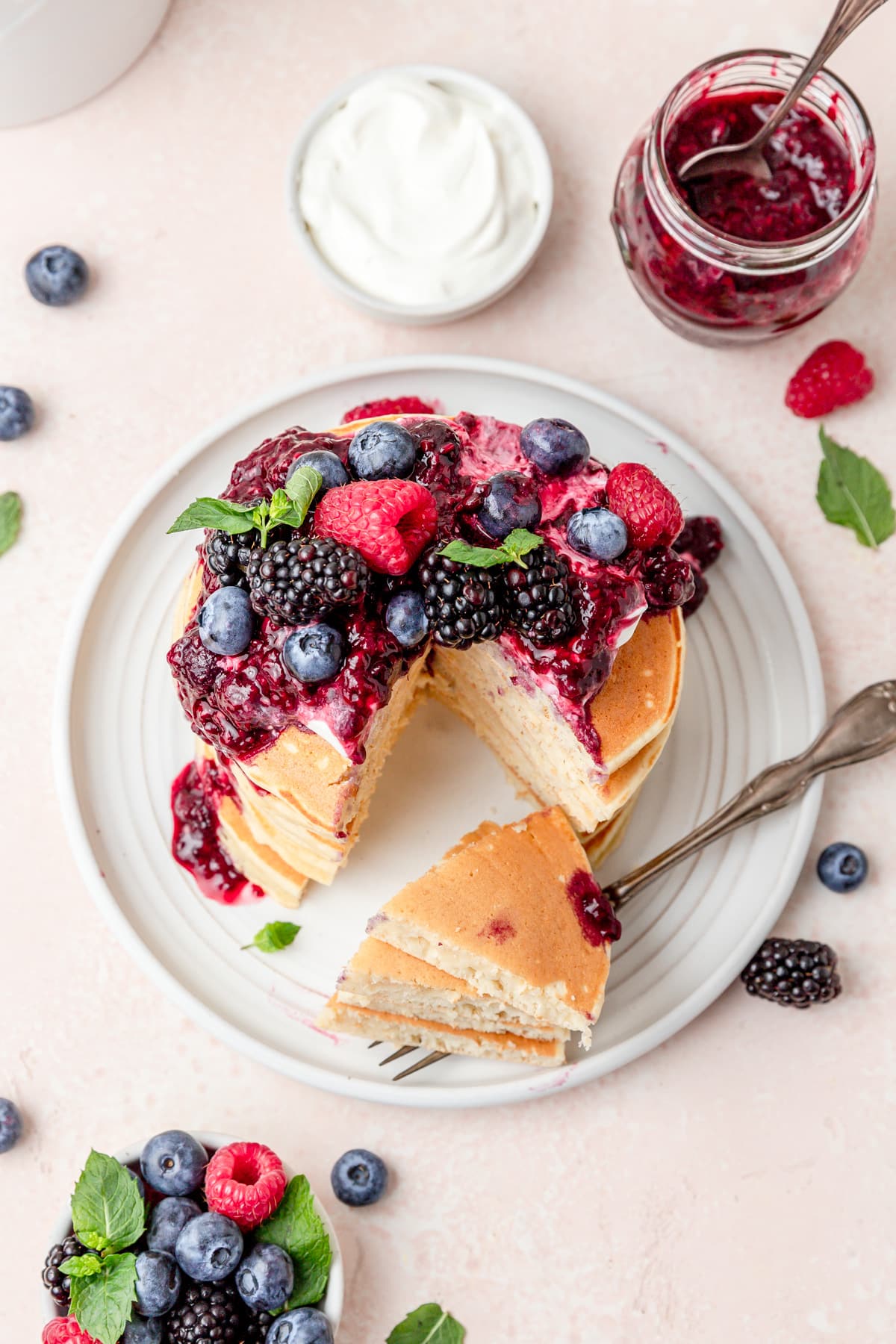 ricotta pancakes topped with whipped cream, berry sauce, and fresh berries.