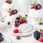 close up of mini pavlovas topped with berry compote and whipped cream.