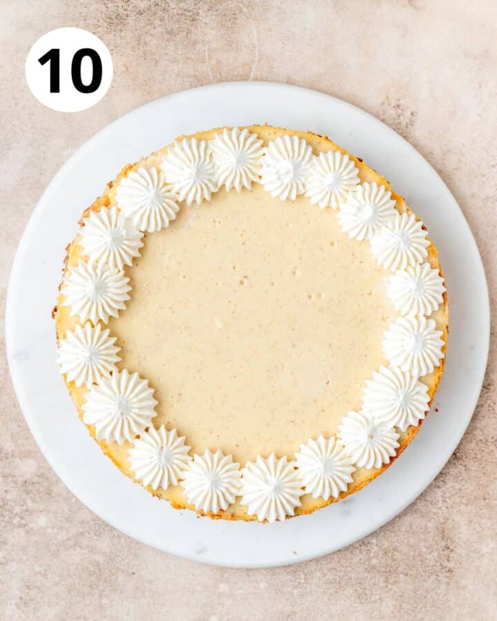 piping whipped cream on top of eggnog cheesecake.