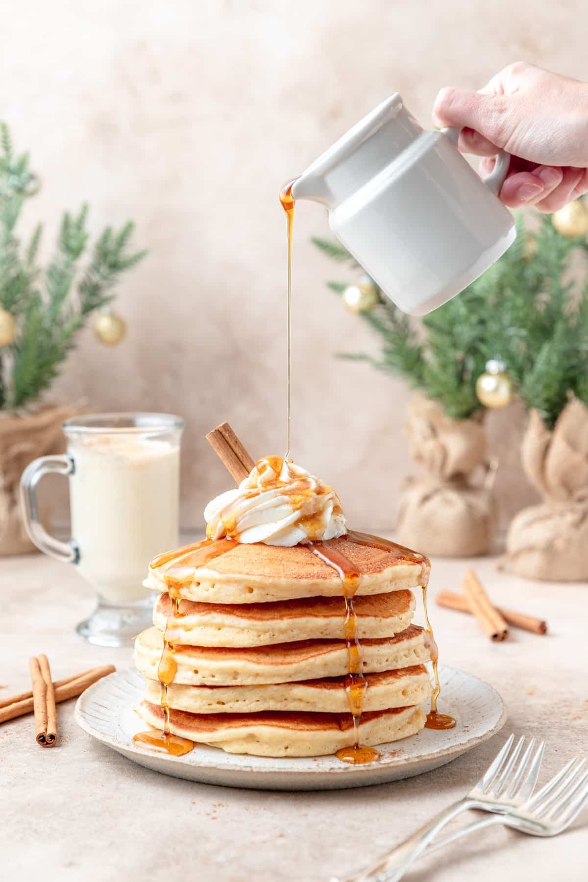 pouring maple syrup on stack of eggnog pancakes.